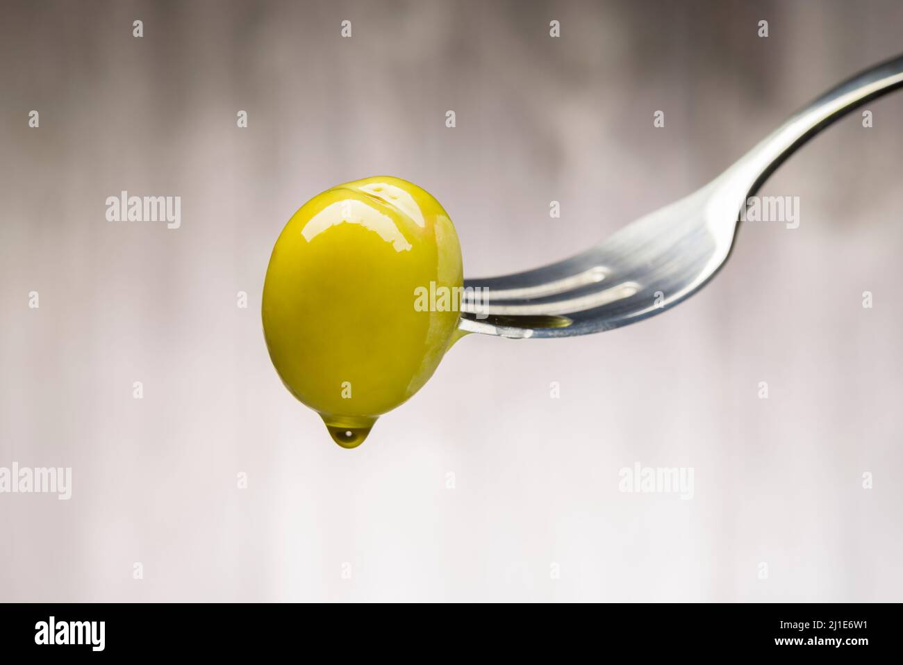 Green olive on fork with dripping oil, on wooden background Stock Photo