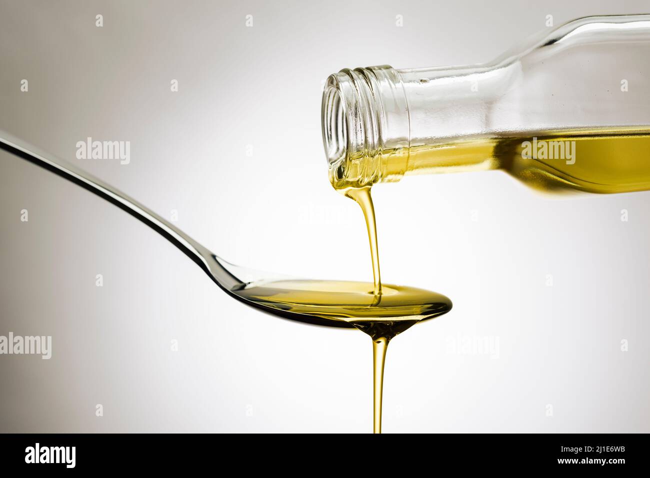 Olive oil bottle pouring oil on spoon, on gradient background Stock Photo