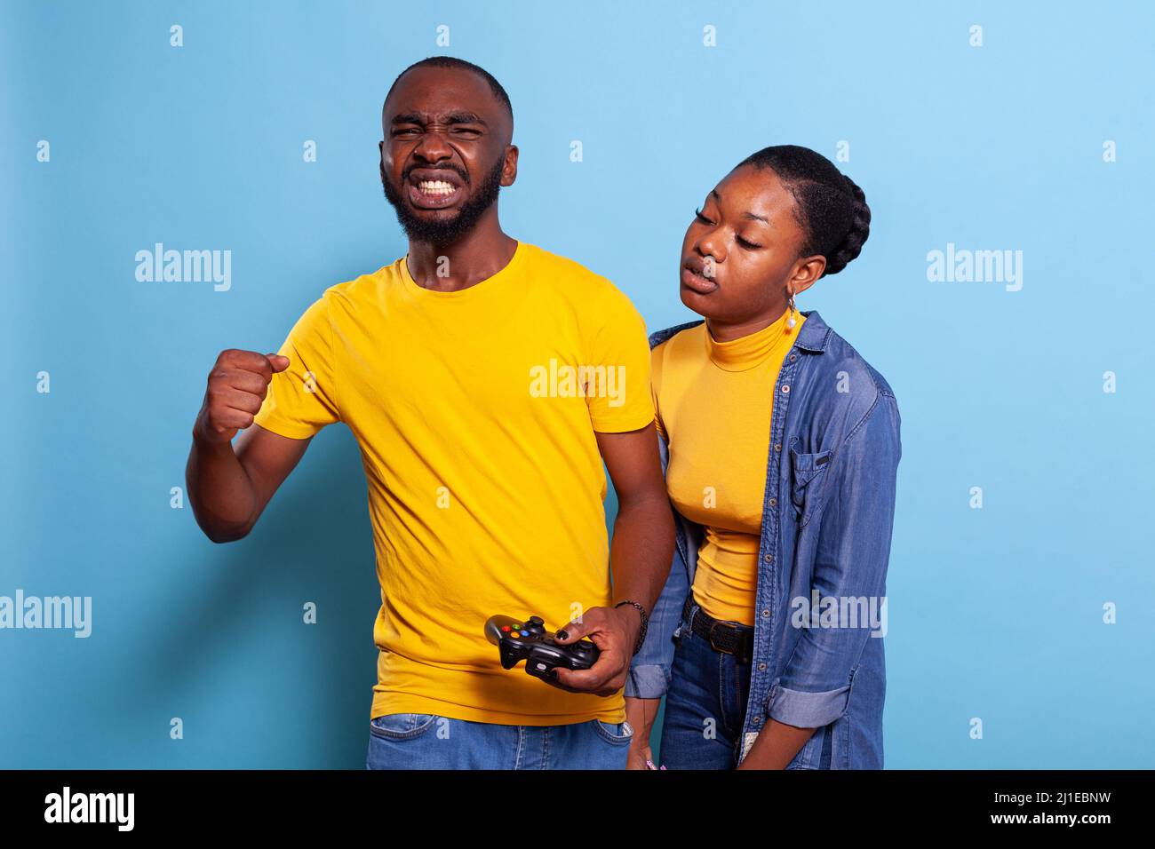 Frustrated couple losing video games on console with joystick in studio. Disappointed boyfriend and girlfriend using controller to play online game, feeling sad about losing in front of camera. Stock Photo