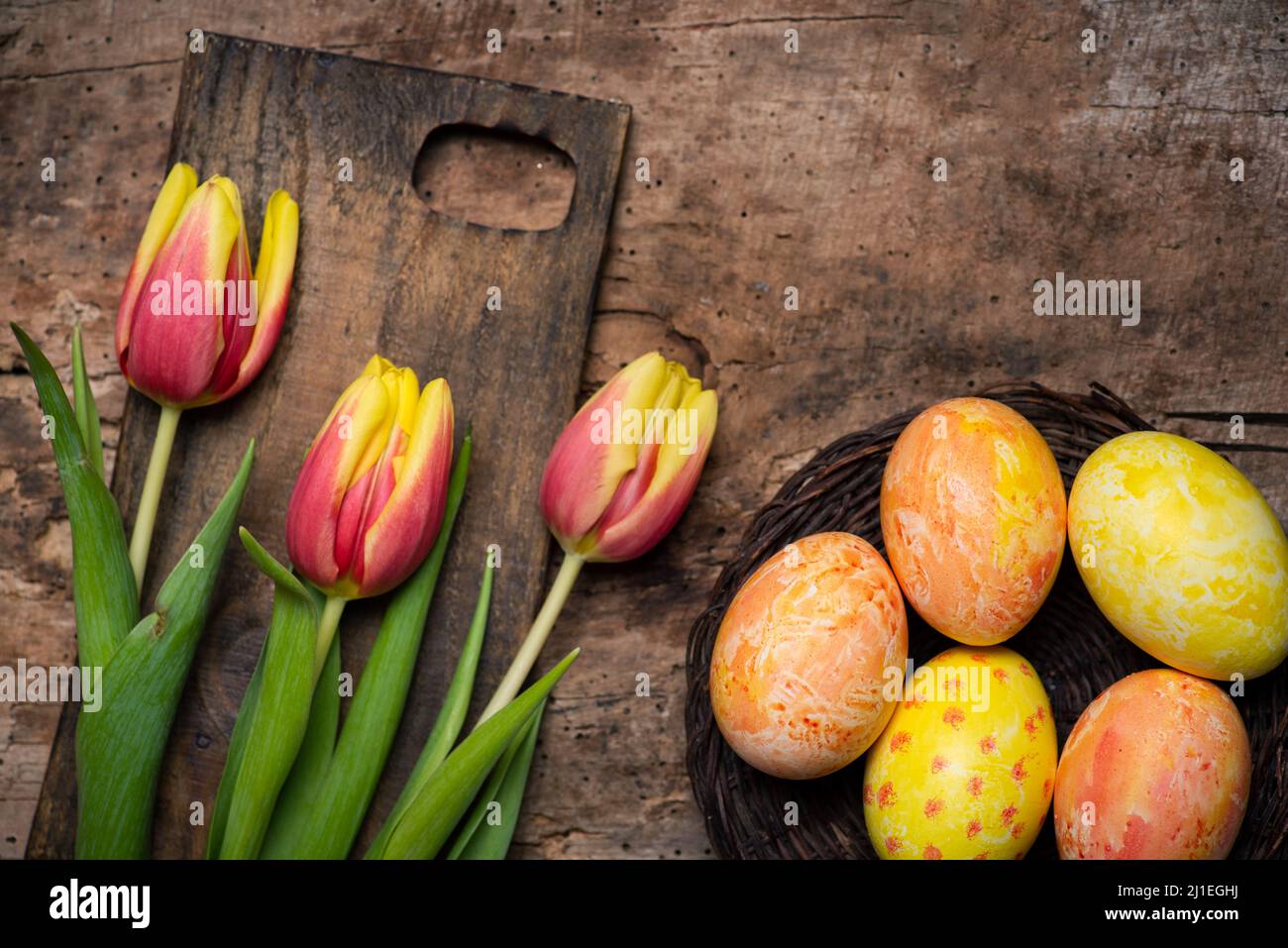 Colorful red and yellow tulips with hand painted Easter eggs on a wooden table tabletop view with copy space Stock Photo