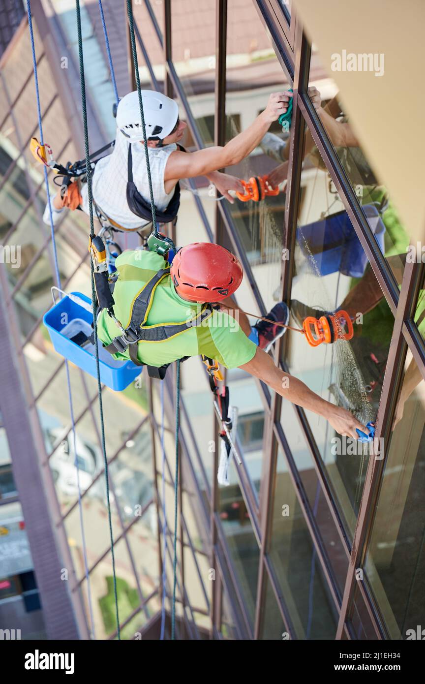 Industrial mountaineering workers washing glass windows of high-rise ...