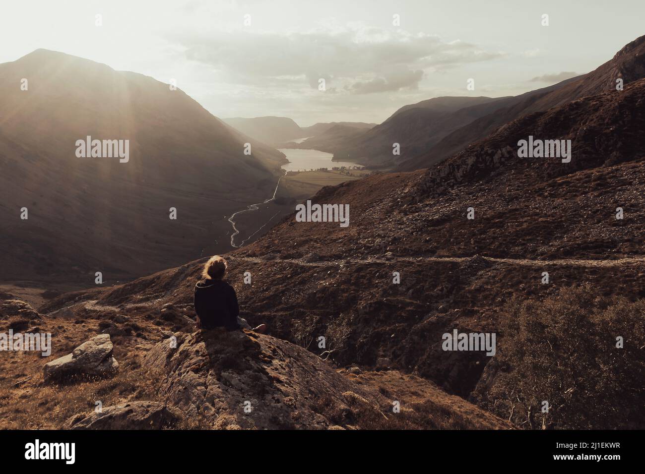 Person sitting on rock and enjoying majestic view on mountain valley in Lake District at sunset. Stock Photo
