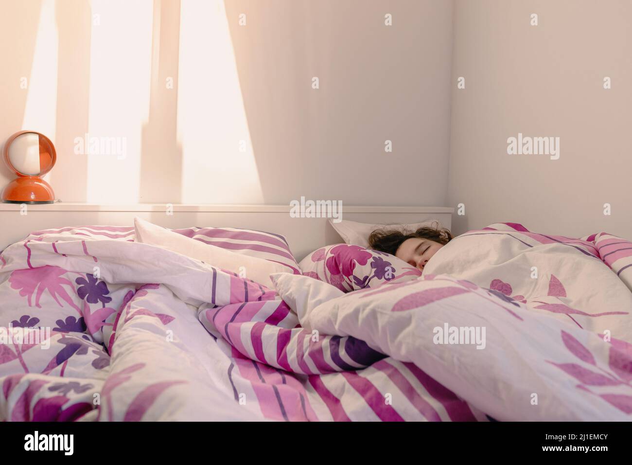 Sleeping girl in comfortable bed, covered with blanket, in rays of