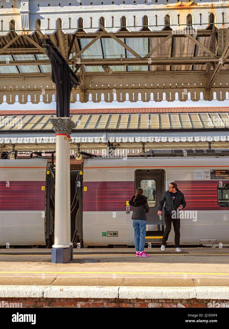 Railway station platform with a train carriage . Overhead is an historic canopy and passengers