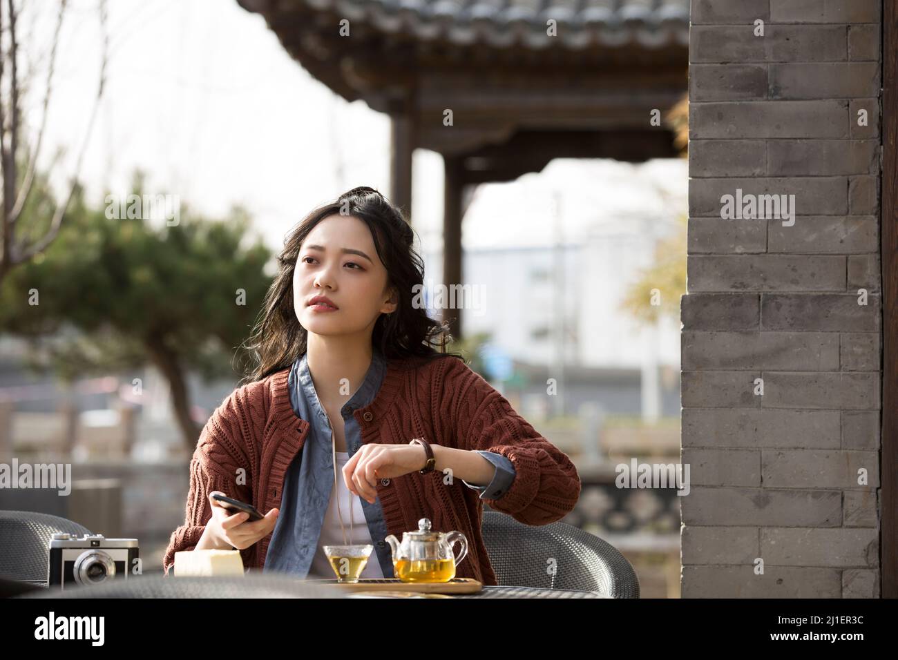 Chinese college student calling friend and enjoying afternoon tea in sidewalk cafe - stock photo Stock Photo
