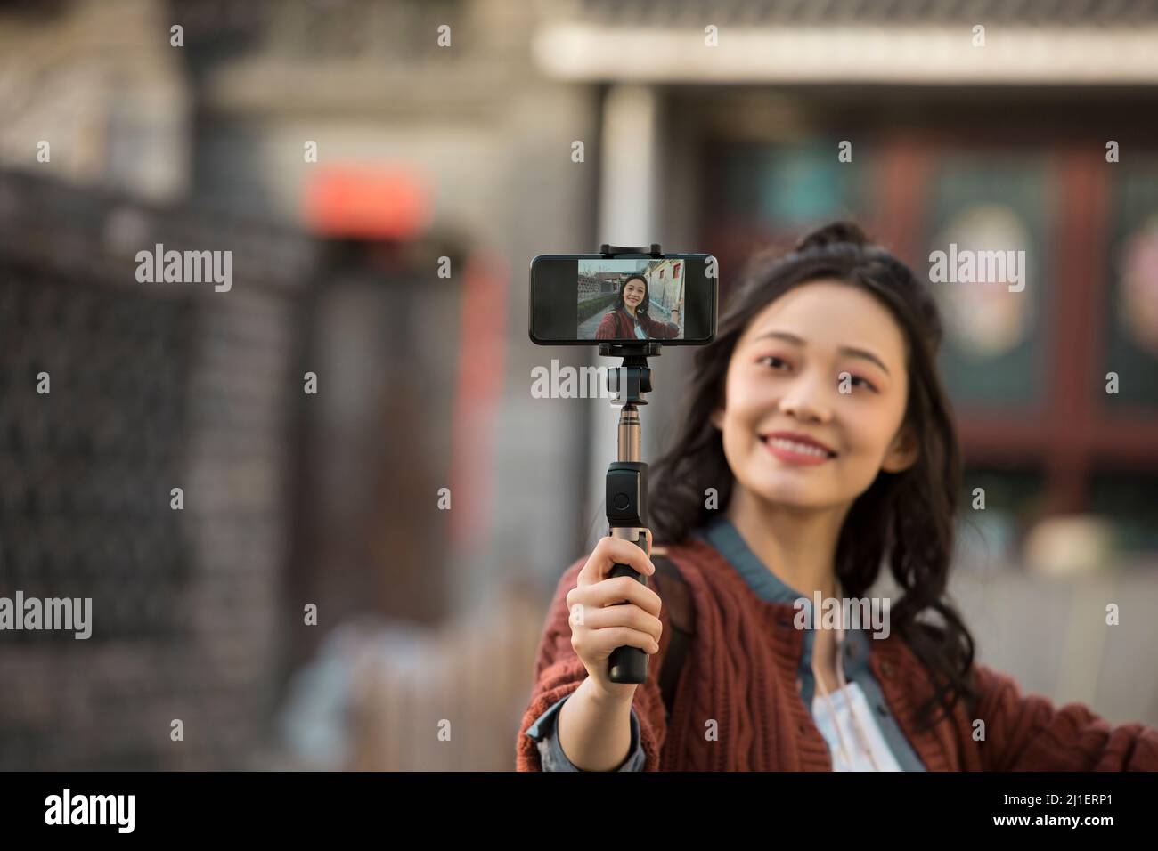 Young female tour guide holding selfie stick to stream live video on smart phone - stock photo Stock Photo