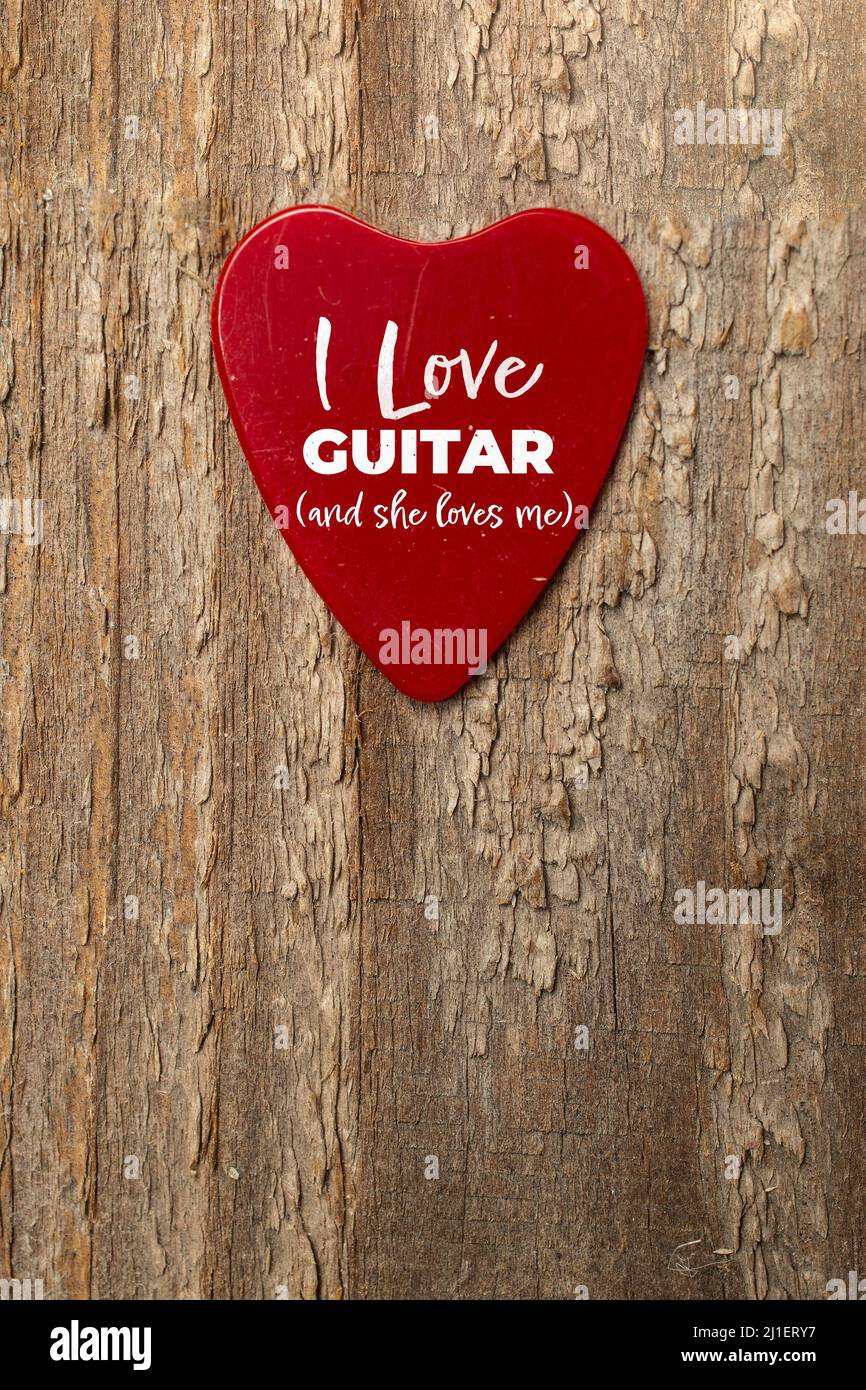 Red heart shaped guitar pick on wooden table with text I love guitar and she loves me Stock Photo