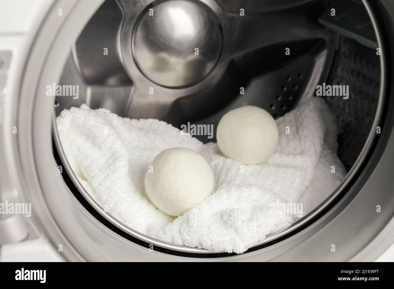 Using wool dryer balls for more soft clothes while tumble drying in washing machine concept. Discharge static electricity and shorten drying time. Stock Photo