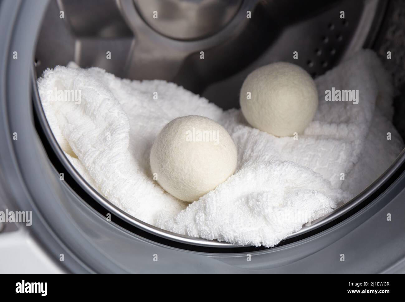 Using wool dryer balls for more soft clothes while tumble drying in washing machine concept. Discharge static electricity and shorten drying time. Stock Photo