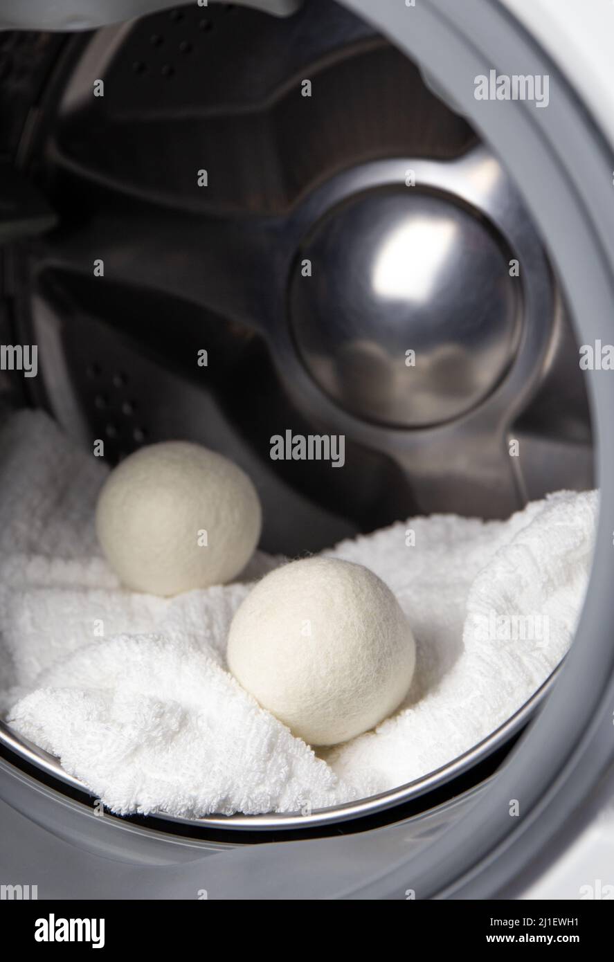 Using wool dryer balls for more soft clothes while tumble drying in washing machine concept. Discharge static electricity and shorten drying time. Stock Photo