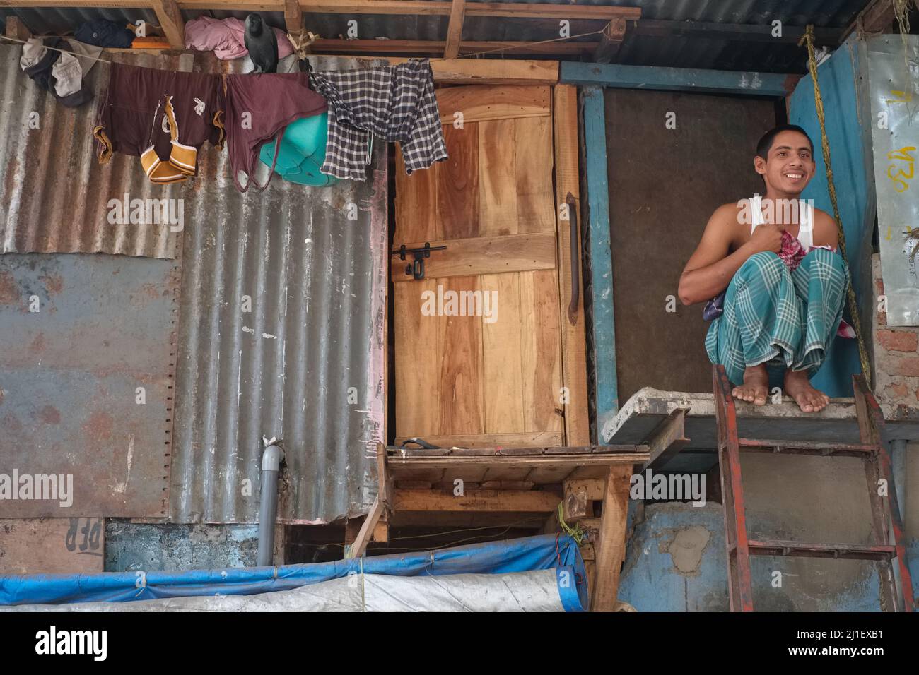 A migrant ostentatiously from West Bengal sitting on the second floor of a jhopra / jhopri (hut, makeshift house) in a slum area of Mumbai, India Stock Photo