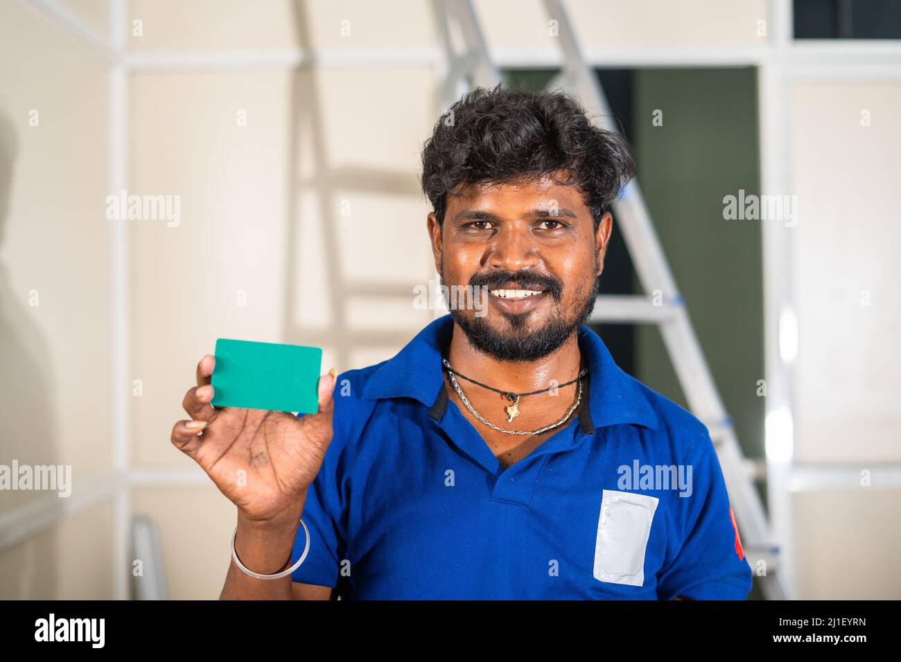 worker showing green card by looking at camera at construction site- concept of employee id, maintenance or renovation service and promotion. Stock Photo