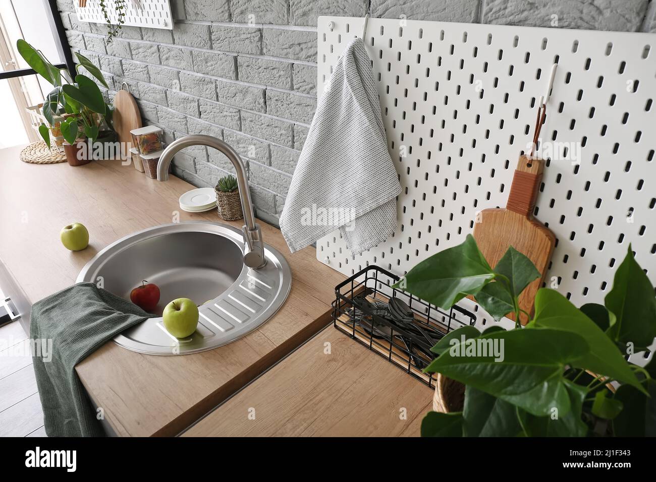 Wooden counter and pegboard with kitchen utensils near grey brick wall