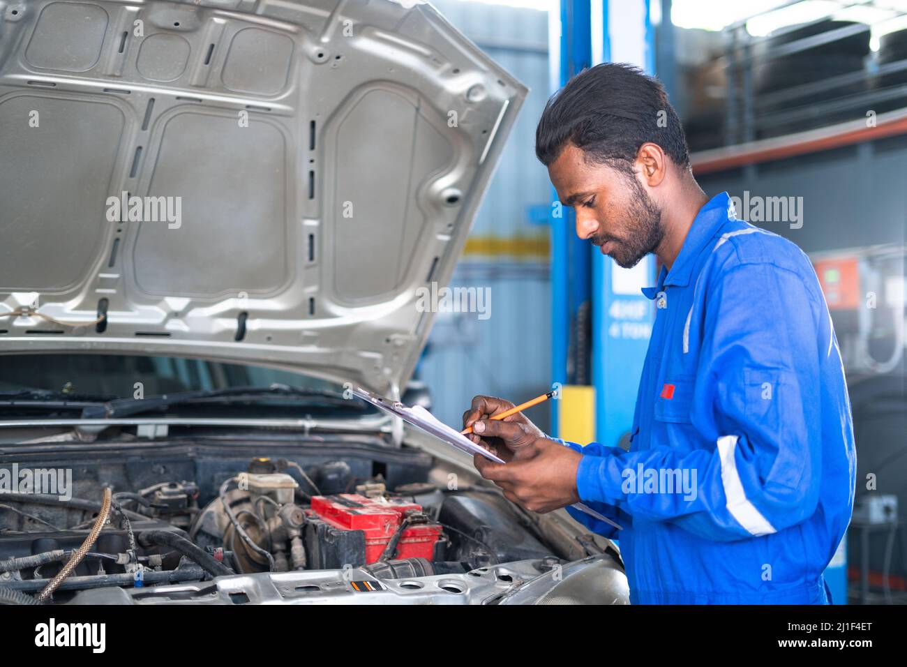 focus on hands Car mechanic noting repair parts during open car hood engine repair at garage - concept of customer report, professional worker and Stock Photo