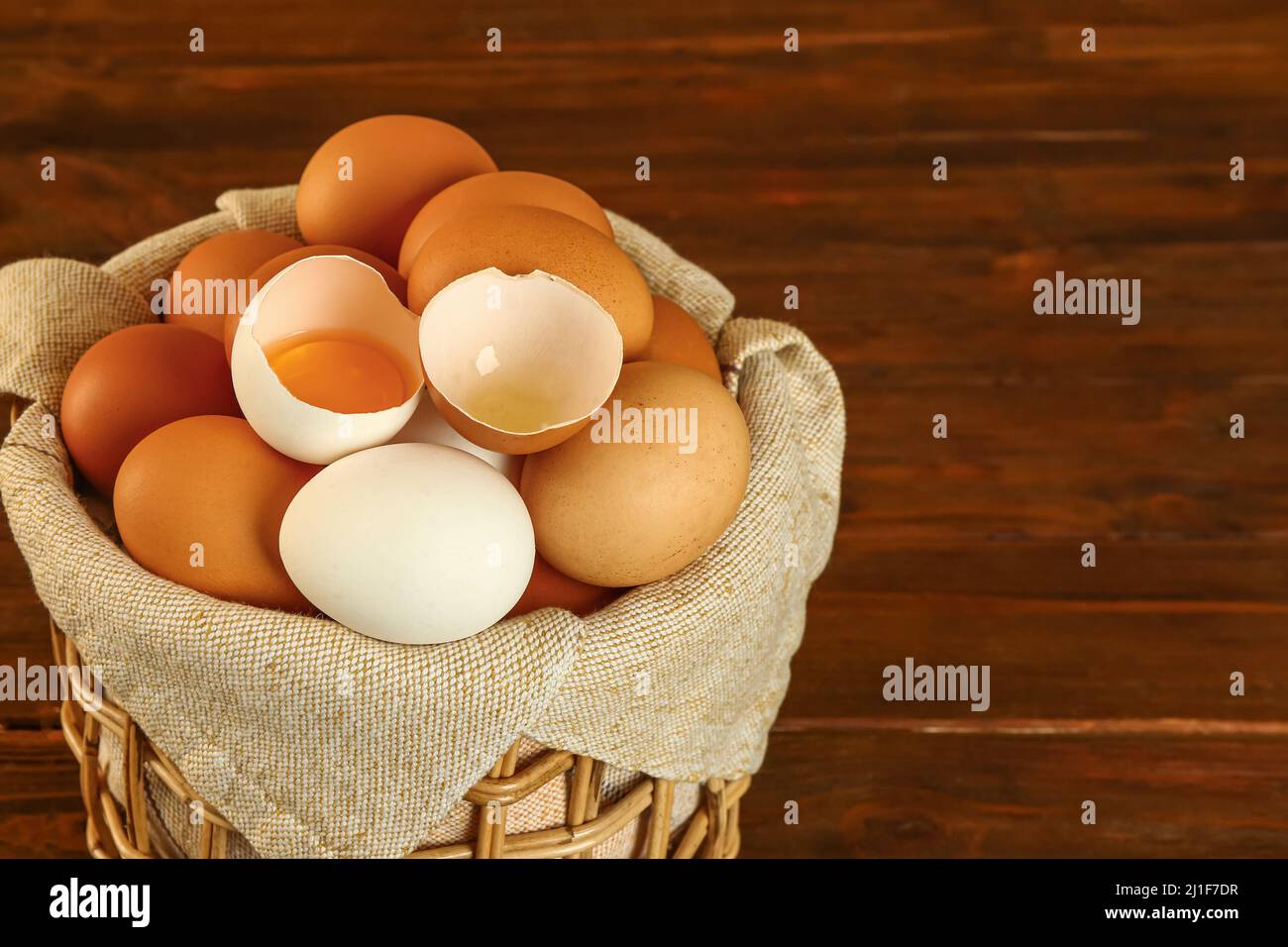Wicker basket with fresh chicken eggs on wooden background, closeup ...
