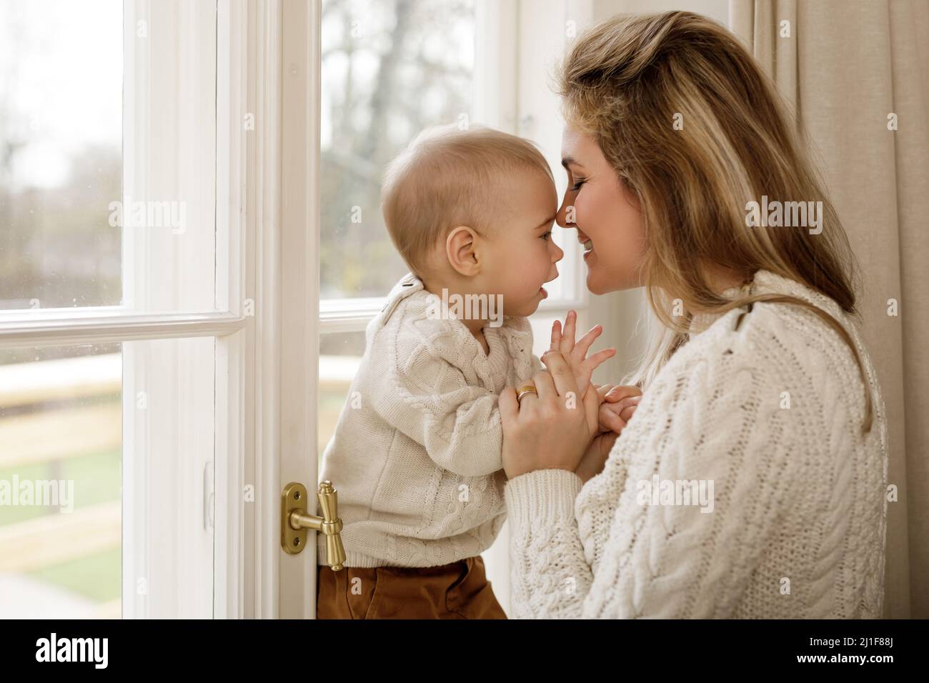 Mother and her little baby son wearing warm sweaters standing by the