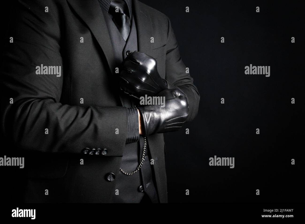 Portrait of Strong Man in Dark Suit Pulling on Black Leather Gloves. Concept of Mafia Hitman or Gentleman Assassin Stock Photo