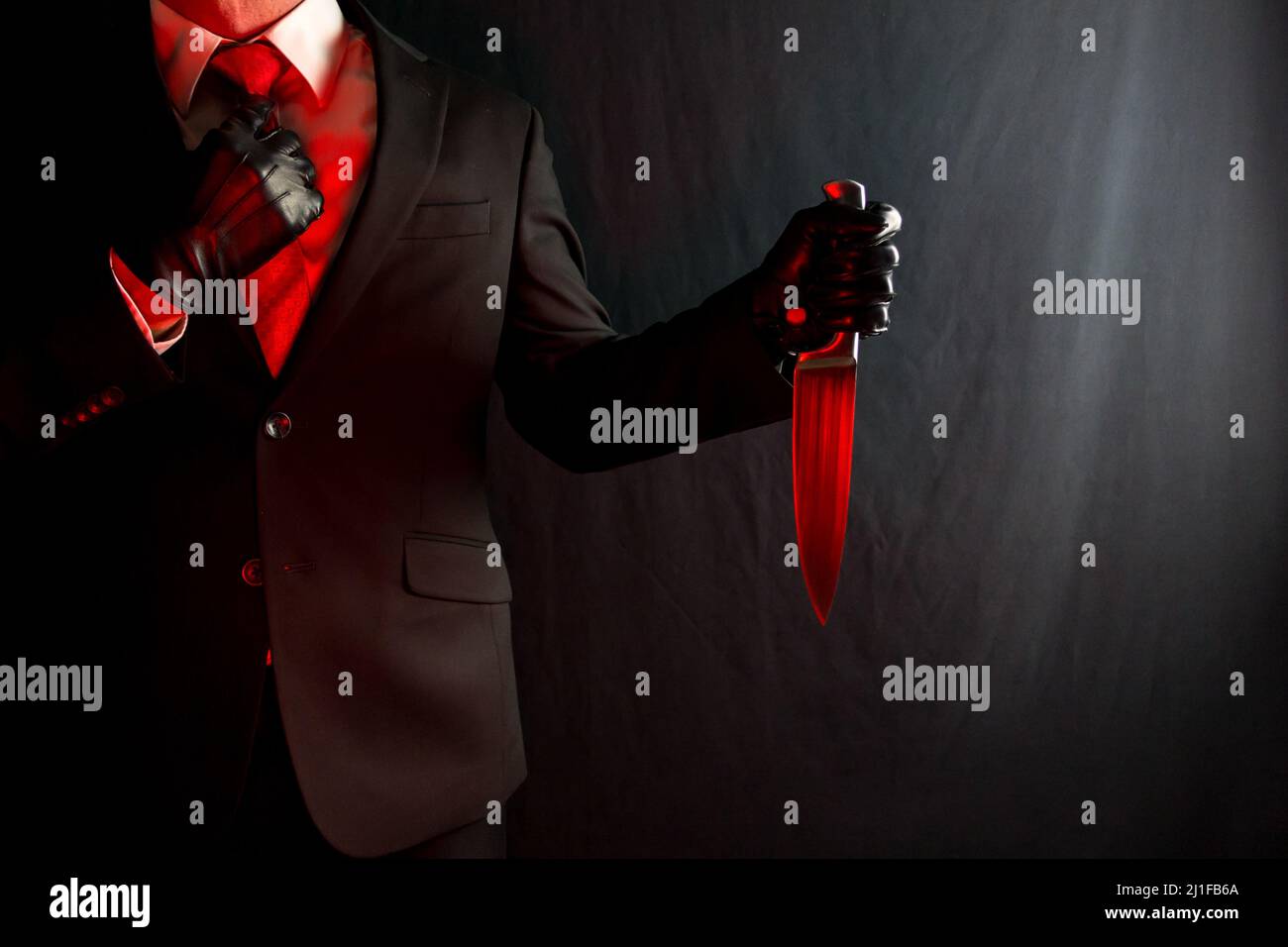 Portrait of Businessman in Dark Suit Holding Bloody Red Knife on Black Background. Concept of Horror Movie Killer and Stylish Assassin. Stock Photo