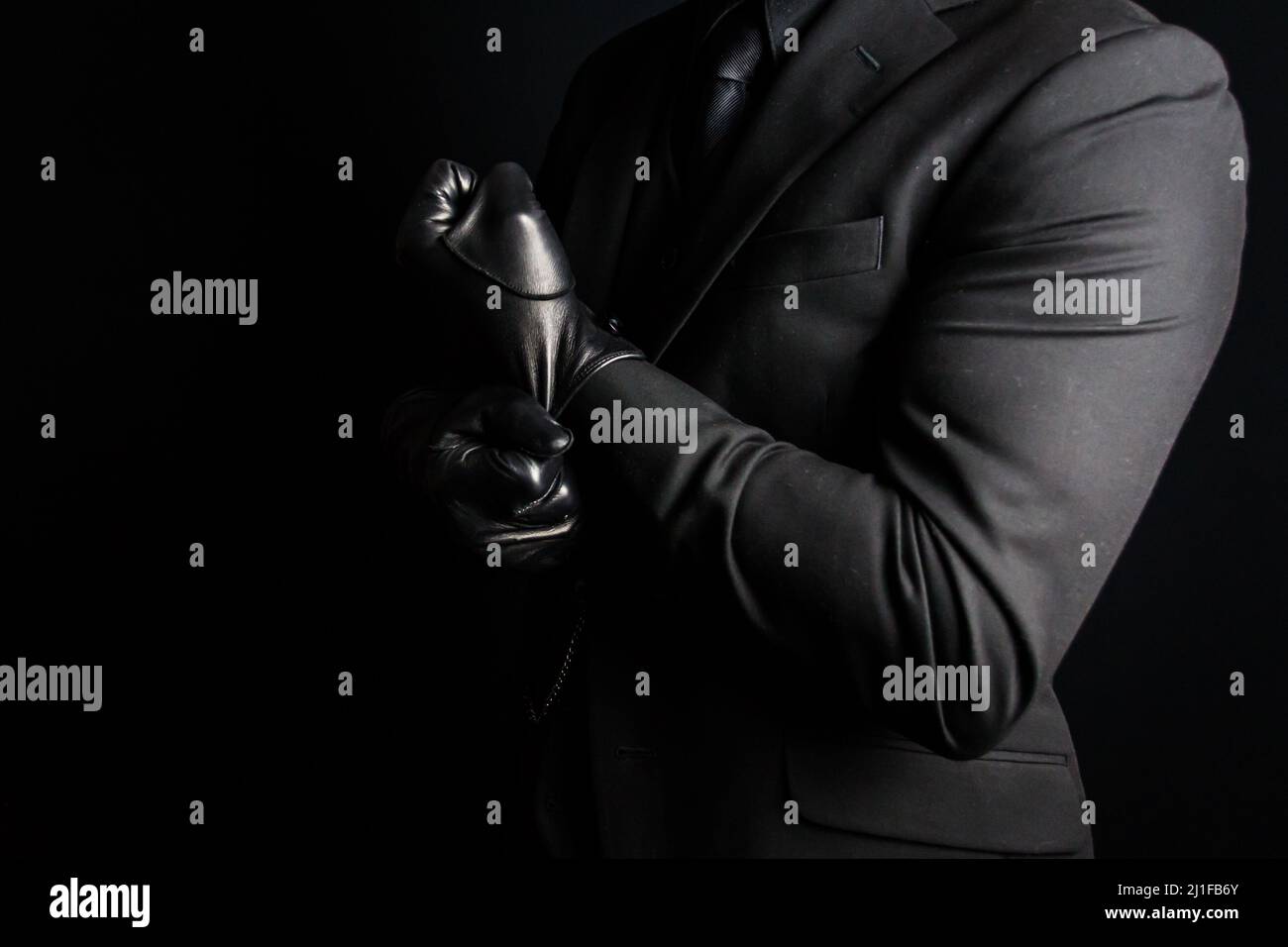 Portrait of Man in Dark Suit Pulling on Black Leather Gloves. Mafia Hitman Concept. Stock Photo