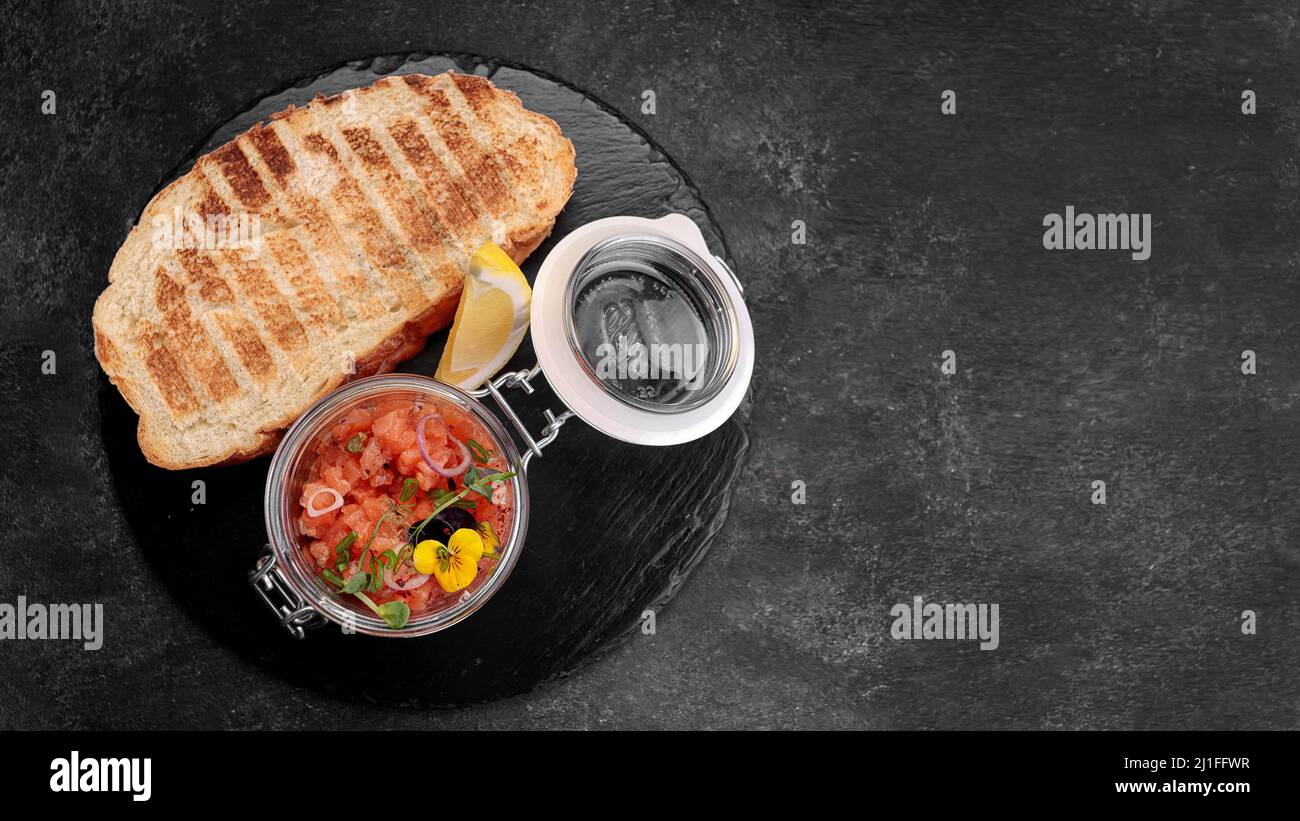 Salmon tartar with toast, in a glass jar, on a dark background Stock Photo