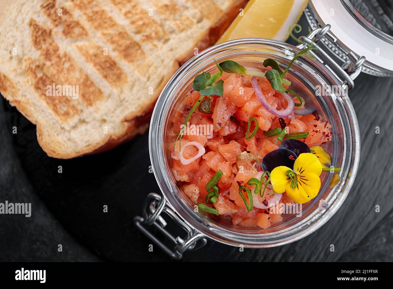 Salmon tartar with toast, in a glass jar, on a dark background Stock Photo