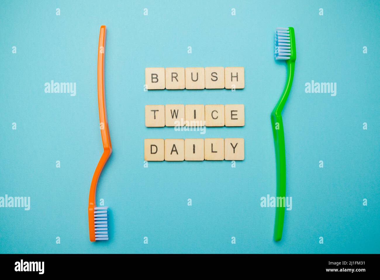 Oral and dental health concept showing two toothbrushes with a sign reading brush twice daily  on a blue coloured background Stock Photo