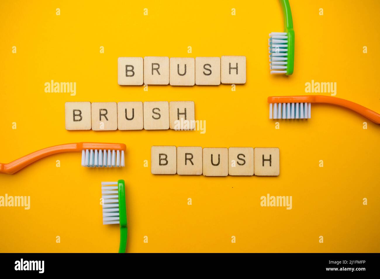 Oral and dental health concept showing four toothbrushes and a sign reading Brush Brush Brush on a yellow coloured background Stock Photo