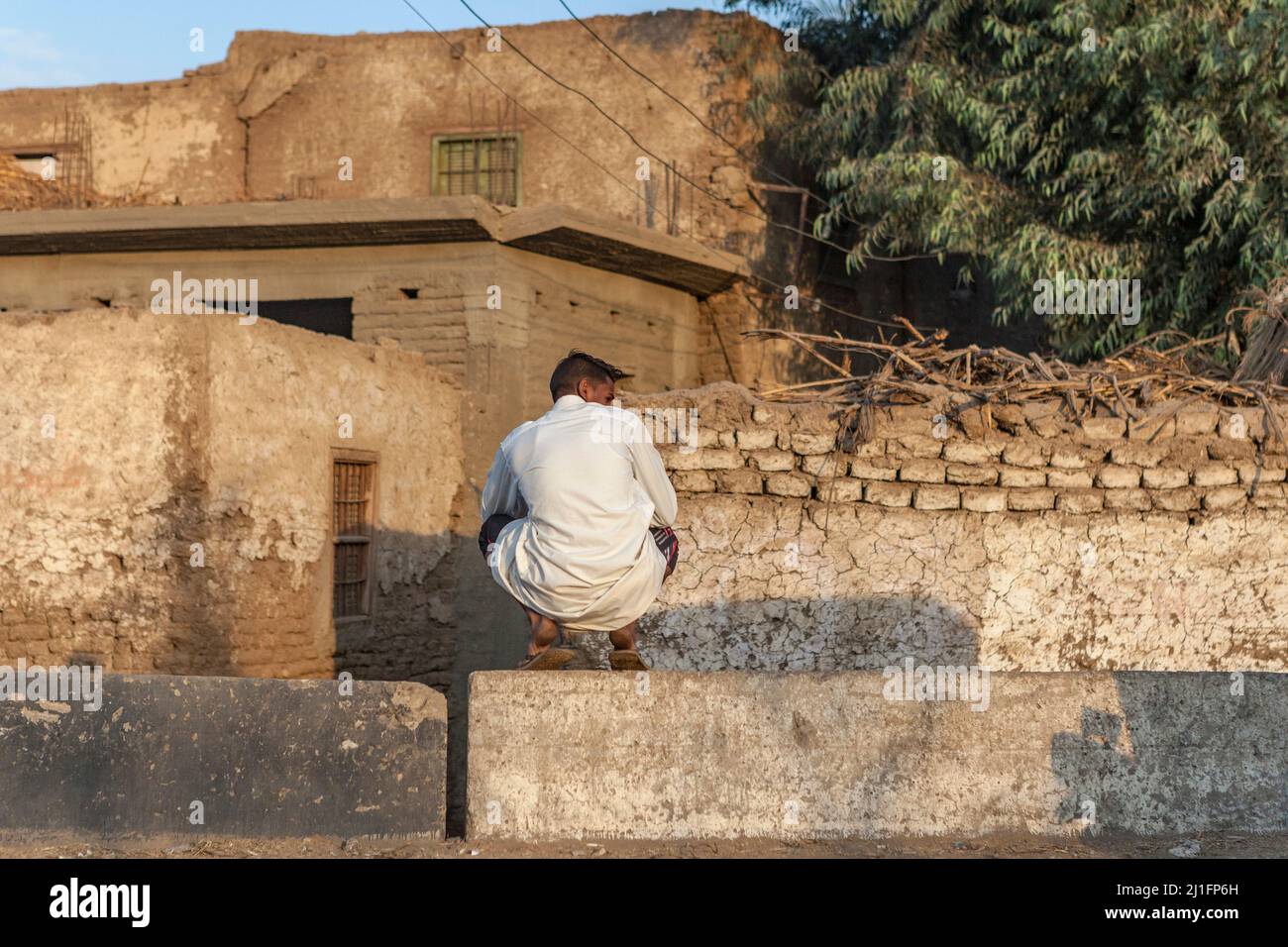 Local man sitting at the side of the road, Qena, Egypt Stock Photo