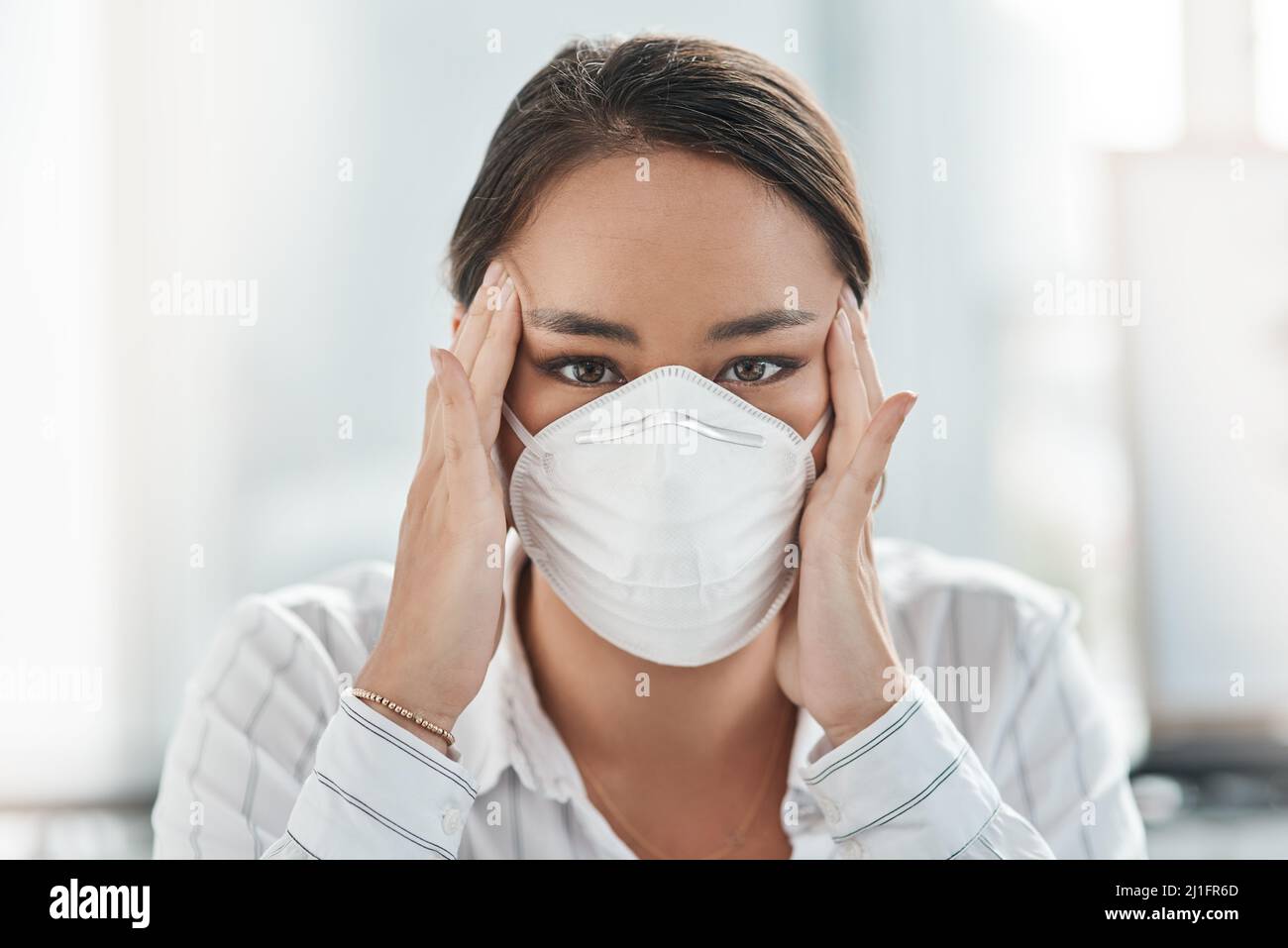 How much more of this do we have to face. Shot of a masked young businesswoman looking stressed while working in a modern office. Stock Photo