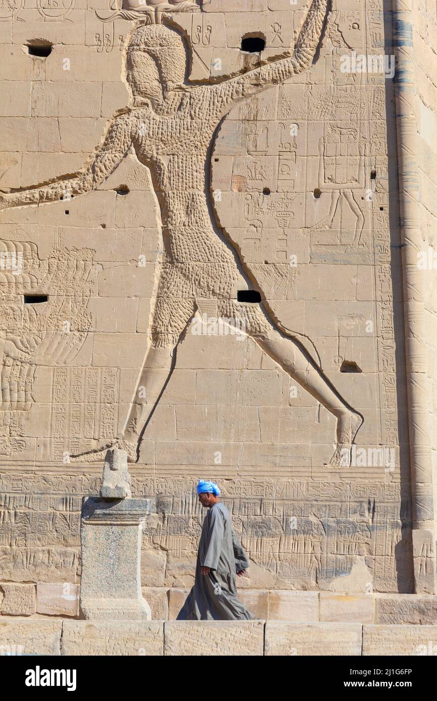 Local Egyptian walking in front of the first pylon of the Temple of Isis at Philae where Ptolemy XII Neos Dionysos is depicted smiting his enemies Stock Photo