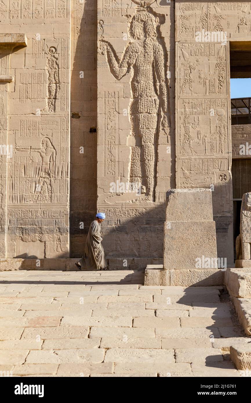 Local walking past the defaced carving of the goddess Isis at the Temple of Isis at Philae Stock Photo