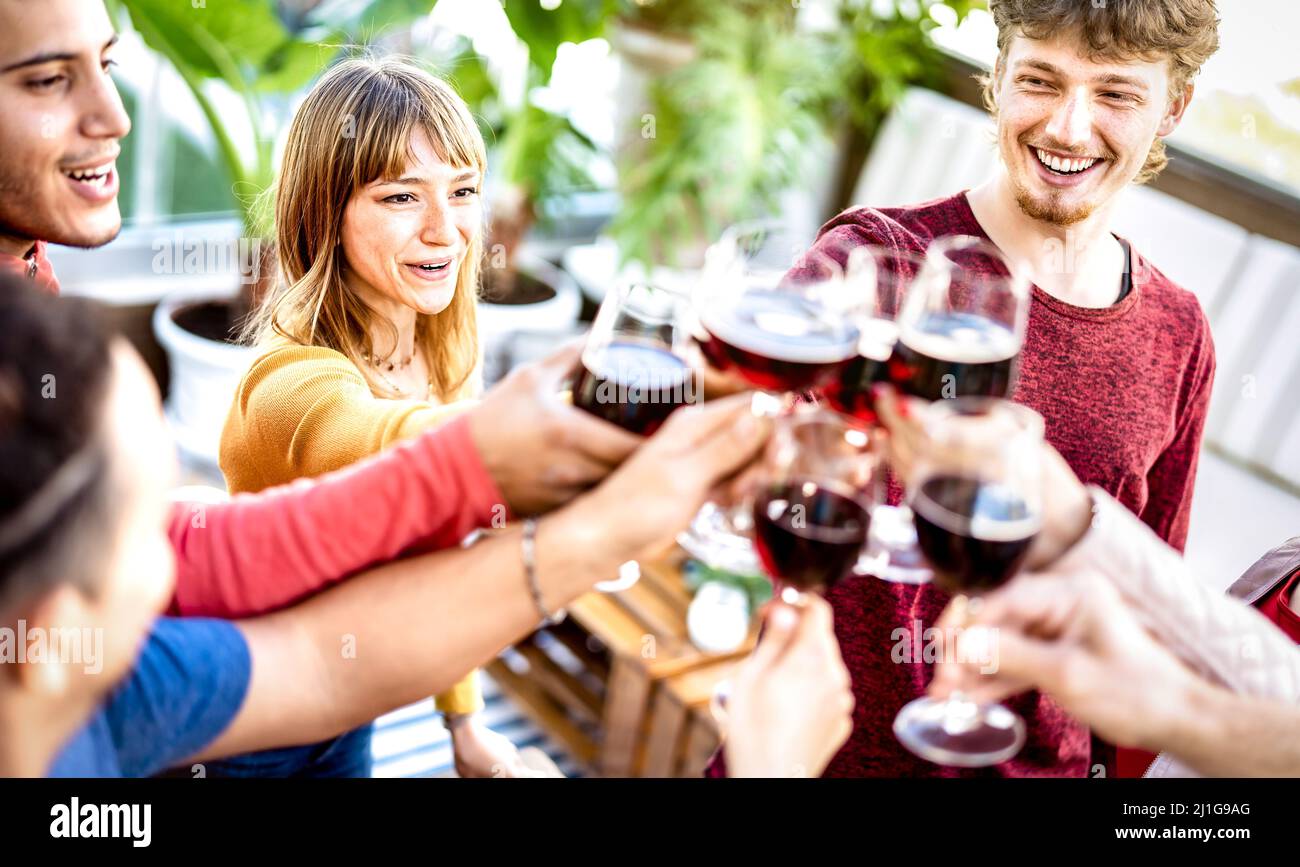 Trendy friends drinking and toasting red wine at rooftop party - Young people having fun together at restaurant winery bar on happy hour Stock Photo