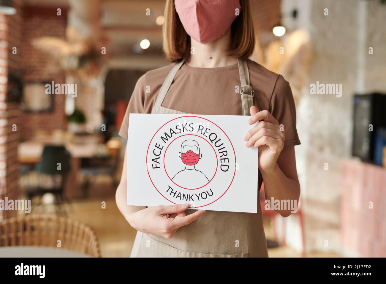 Horizontal shot of unrecognizable cafe worker standing alone holding Face Mask Required sign Stock Photo