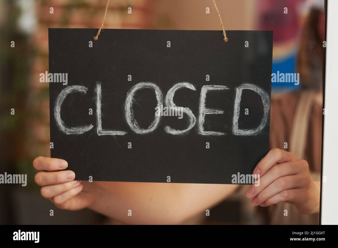 Horizontal close-up through door glass shot of unrecognizable woman closing cafe for break Stock Photo