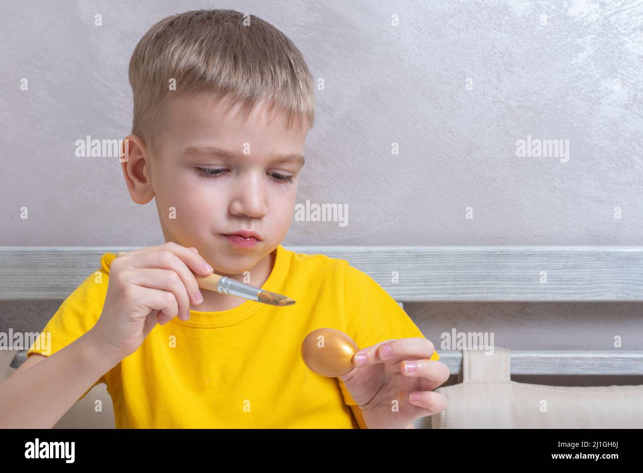 A little blond boy paints eggs for the Easter holiday at home. The child has fun and celebrates the holiday. DIY Easter eggs concept. Stock Photo