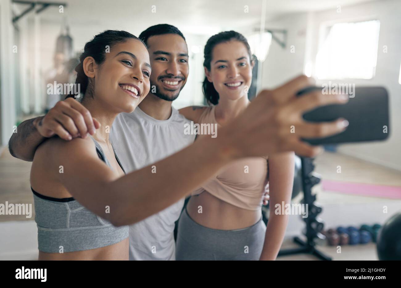 Online to spread some fitness inspiration. Shot of three young athletes taking a selfie while standing together in the gym. Stock Photo