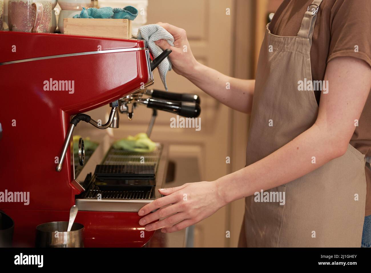 Medium section side view shot of unrecognizable female cafe worker wearing apron cleaning modern espresso coffee machine Stock Photo