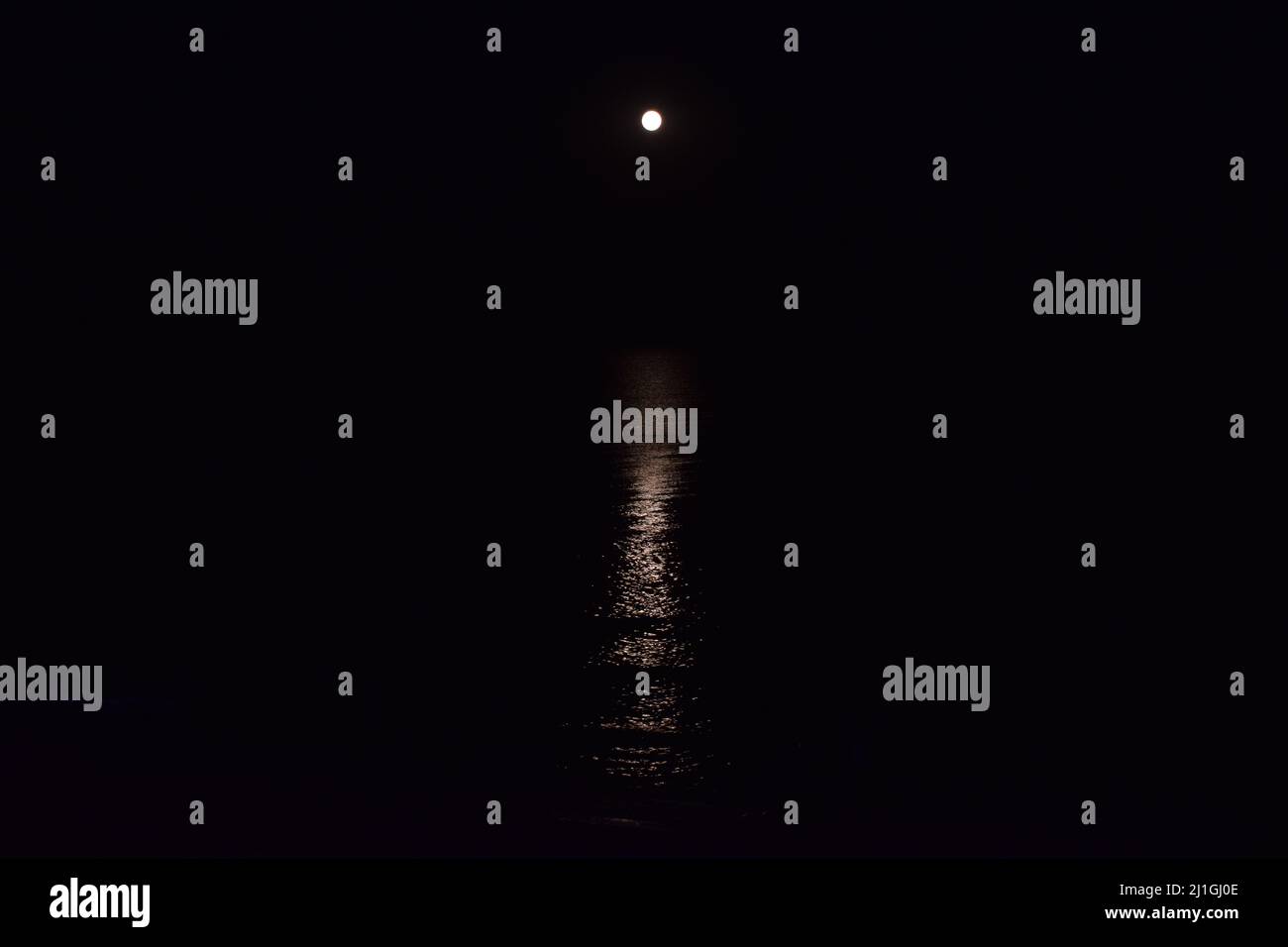 The full moon on the beach. The moon track is reflected in the water. The night moon came up over the water. Full moon on the beach. Full moon at nigh Stock Photo