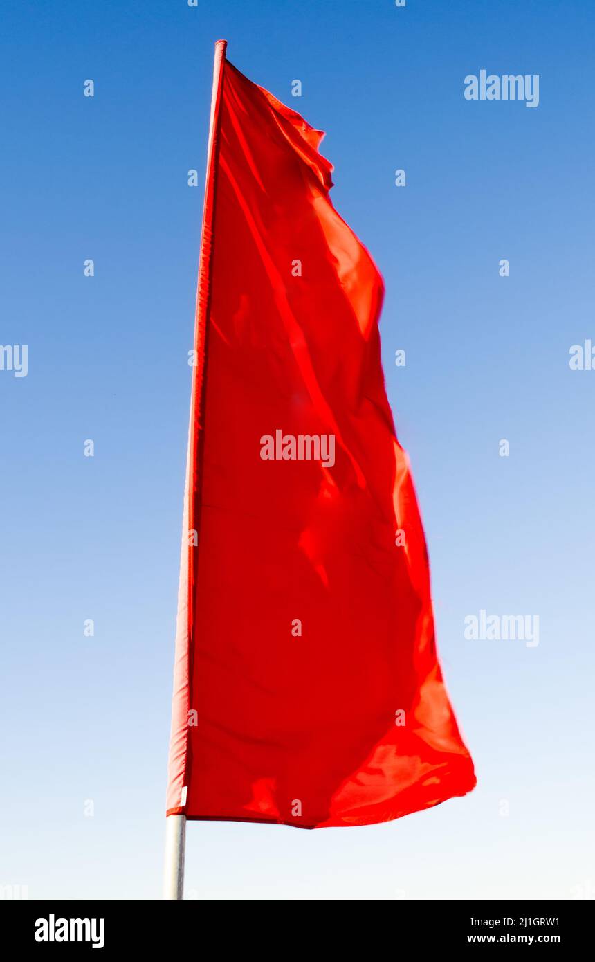 Red flag of rectangular shape elongated fluttering in the wind on the ...