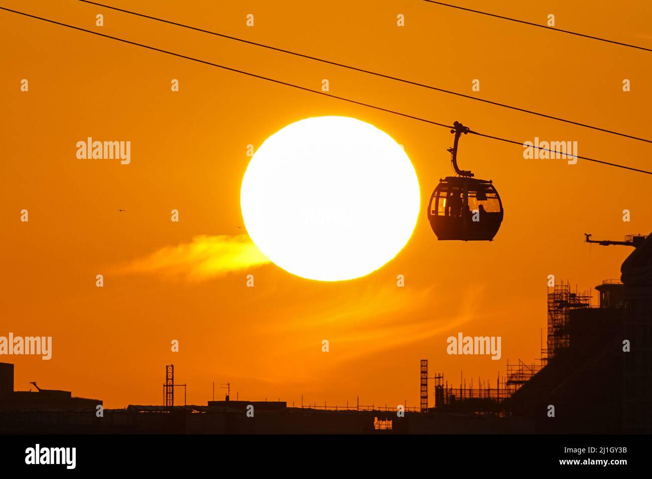 London, UK. 25th Mar, 2022. UK Weather: Sun sets behind the Emirates Air Line cable car. Credit: Marcin Rogozinski/Alamy Live News Stock Photo