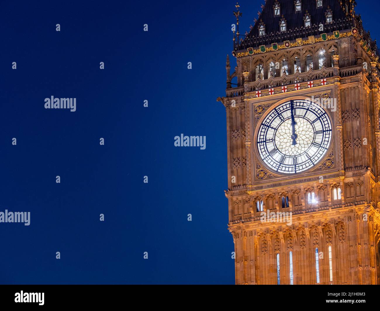 Big Ben at midnight. The iconic London landmark clock tower at exactly 12 o'clock; illuminated and set against a clear blue night sky with copy space. Stock Photo