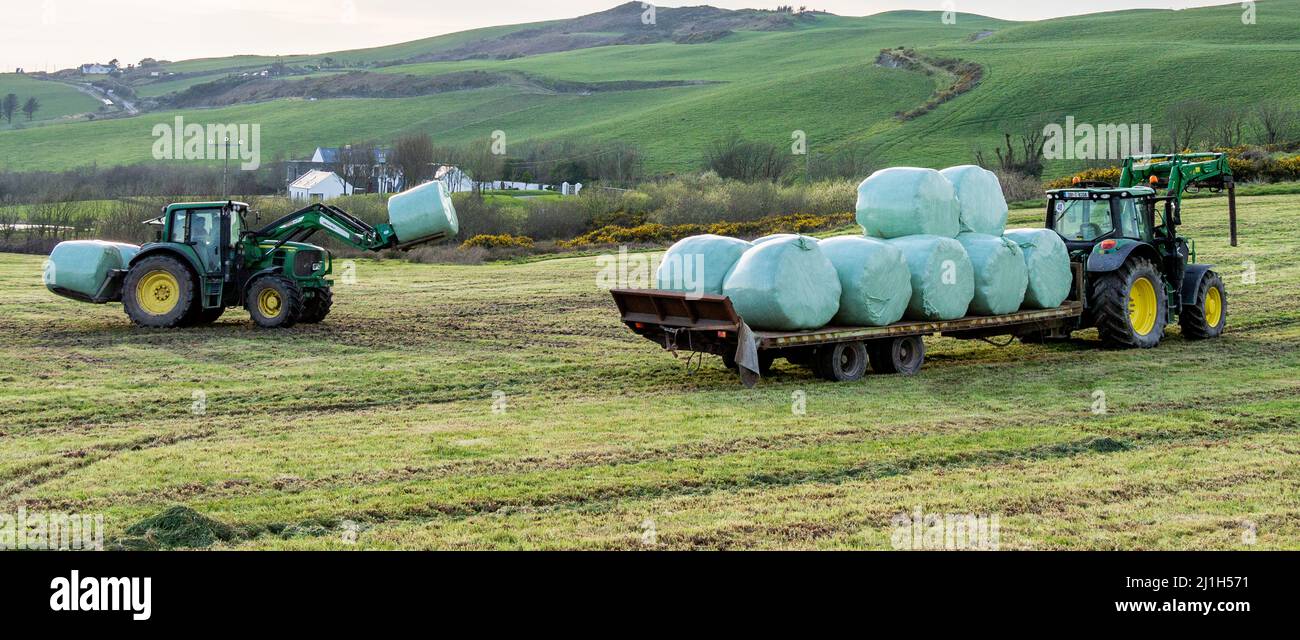 Tractor loading silage bales onto trailer in Irish Countryside Stock Photo