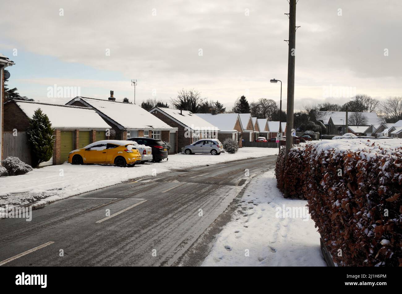 Bungalows along a snow-covered road through a suburban UK housing estate in winter Stock Photo