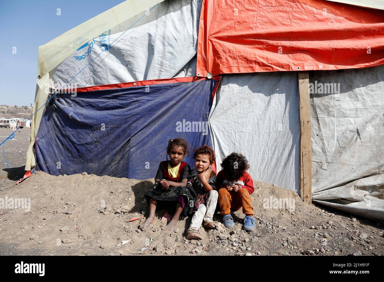Sanaa, Yemen. 25th Mar, 2022. Children sit in front of a tent at the Dharawan camp for internally displaced persons (IDPs) near Sanaa, Yemen, on March 25, 2022. Yemen has been mired in a civil war since late 2014 when the Iran-backed Houthi militia seized control of several northern provinces and forced the Saudi-backed Yemeni government of President Abd-Rabbu Mansour Hadi out of the capital Sanaa. Credit: Mohammed Mohammed/Xinhua/Alamy Live News Stock Photo