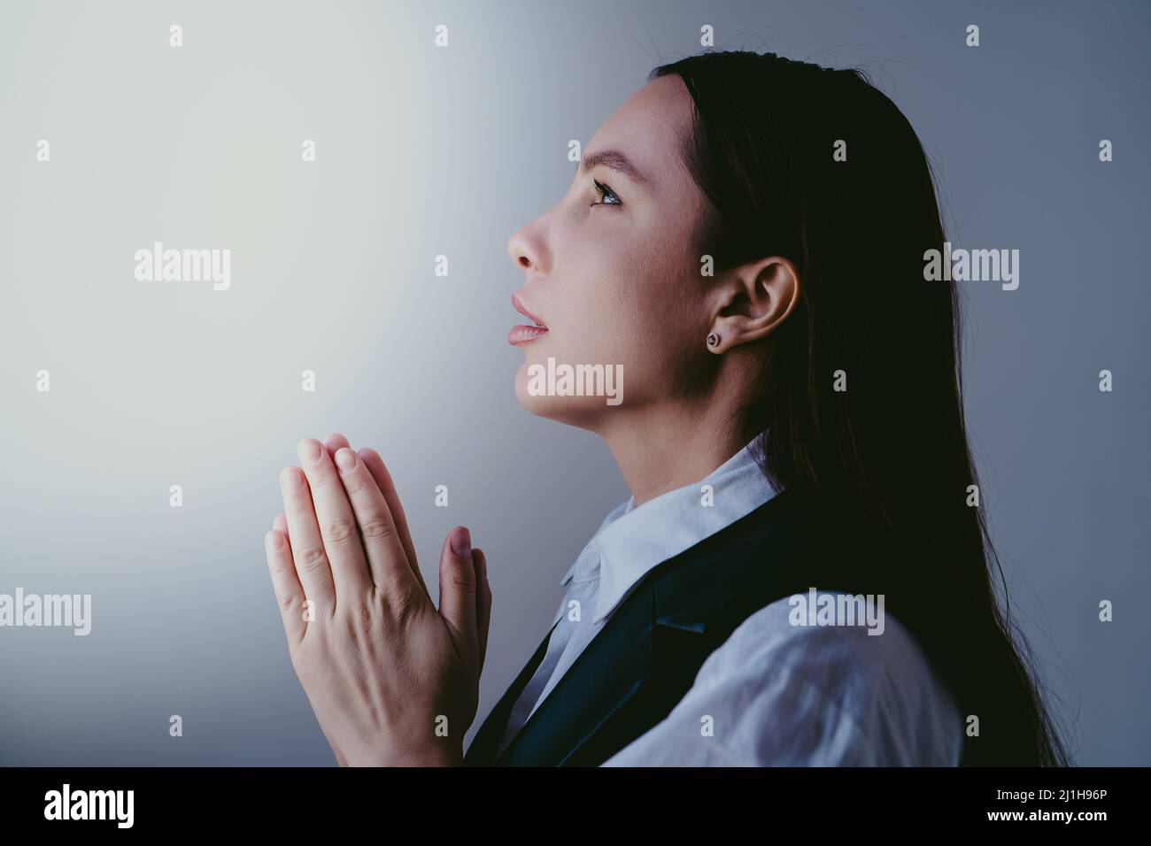Young brunette girl pray to god, close up portrait. Woman folds her hands in prayer. Faith and hope concept. Stock Photo