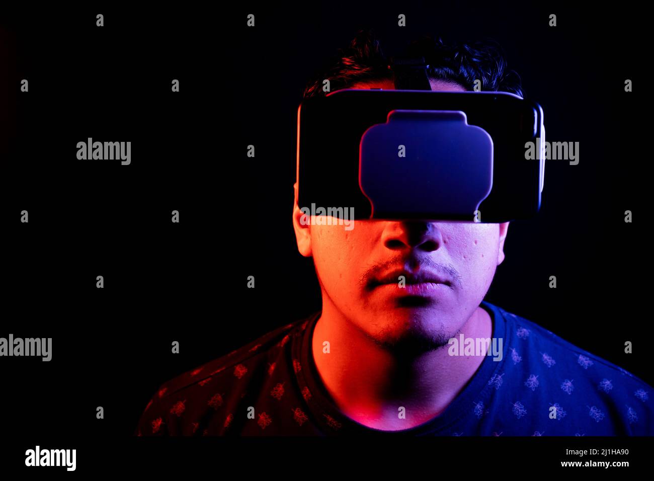 Young latin man using Virtual Reality VR Headset 3D Glasses. Dark backdrop. Low key. Copy space. Stock Photo