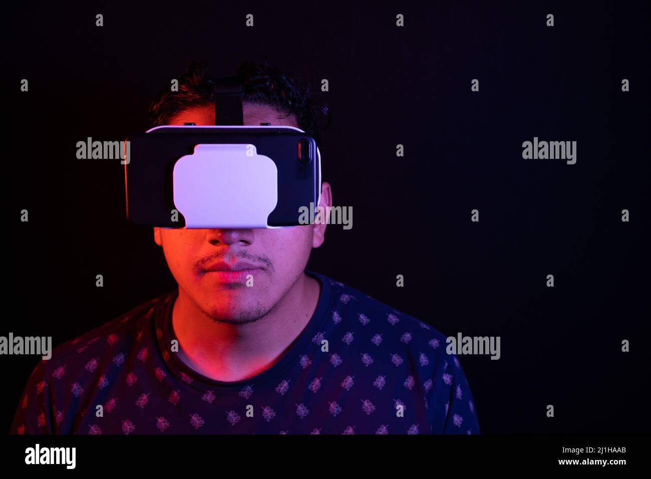 Young latin man using Virtual Reality VR Headset 3D Glasses. Dark backdrop. Low key. Copy space. Stock Photo
