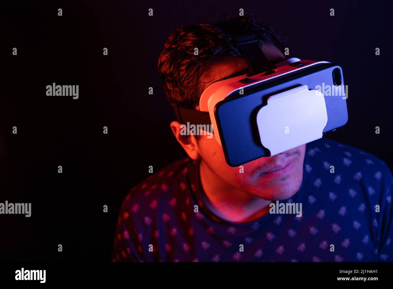 Young latin man using Virtual Reality VR Headset 3D Glasses. Dark backdrop. Low key. Copy space. Stock Photo
