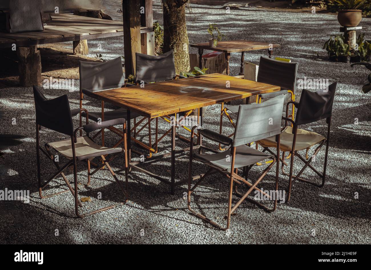 Wooden old table and Empty folding camping chairs in front of the house with nature environment with morning sun rays shine through. Selective focus. Stock Photo