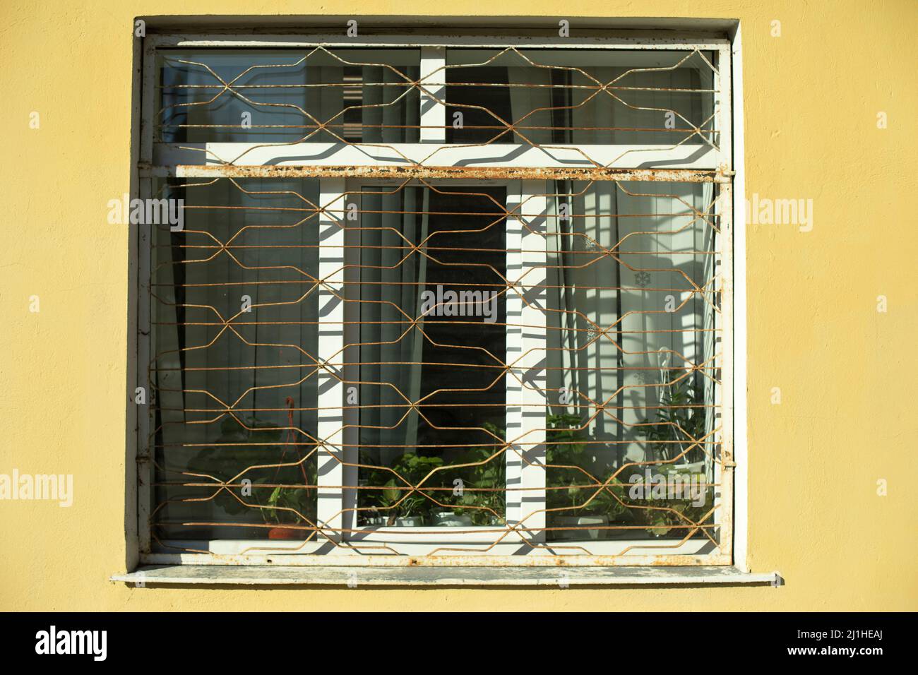 Window with grille. Ground floor of building. Window in yellow wall. Protection against robbers grille made of steel. Stock Photo